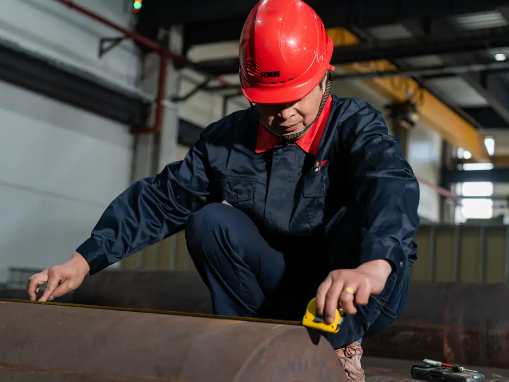 A worker is using a tape measure to inspect a large metal cylinder.