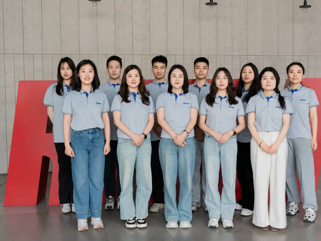 Group photo of RMM employees standing in front of a red RMM logo backdrop