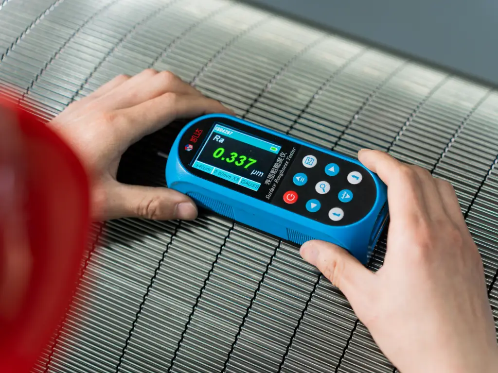 Hands holding a surface roughness tester measuring an RMM corrugating roll.